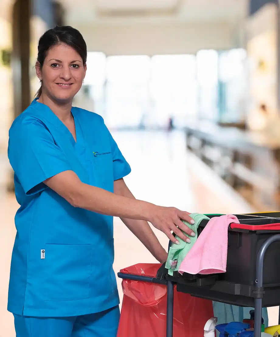 Eine Mitarbeiterin der Gebäudereinigung in Hamburg in blauer Arbeitskleidung mit Reinigungswagen